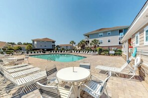 A pool area with lounge chairs and a table, surrounded by buildings with balconies. - Willowbend Unit 834 Condo (North Myrtle Beach)