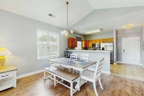 A dining area with a wooden table and chairs, a bench, a lamp, and a window with blinds. - Willowbend Unit 834 Condo (North Myrtle Beach)