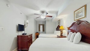 Ein Hotelzimmer mit Bett, Deckenventilator, Fernseher, Nachttisch mit Lampe und Kommode.