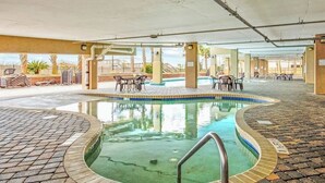 Ein Hallenbad mit gefliestem Sonnendeck, umgeben von Liegestühlen und Tischen.