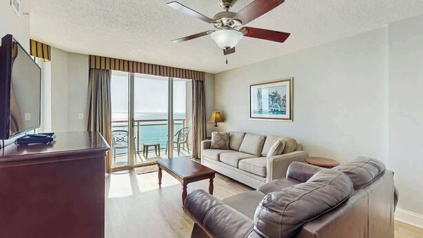 Ein Hotelzimmer mit Balkon, einer Couch, einem Fernseher und einem Deckenventilator.