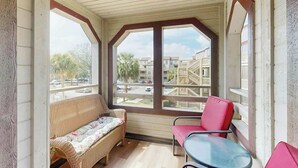 A covered balcony with a wicker sofa, a red chair, and a glass table. - Dunes Pointe Unit B-10 (Myrtle Beach)