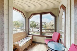 Ein überdachter Balkon mit einem Rattan-Sofa, einem roten Sessel und einem Glastisch.