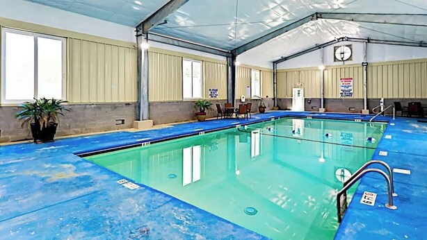 An indoor swimming pool with a covered roof, clear water, and a clock on the wall. - Dunes Pointe Unit B-10 (Myrtle Beach)
