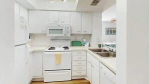A compact kitchen with white cabinetry, a built-in microwave, a stove, and a sink. - Dunes Pointe Unit B-10 (Myrtle Beach)
