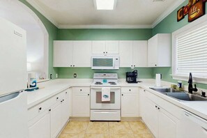 Eine Küche mit weißen Schränken, einer Mikrowelle, einem Backofen, einem Spülbecken und einem Fenster mit Jalousien.