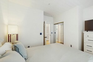 A hotel room with a bed, a bedside lamp, a TV, and a wardrobe. - River Crossing Unit 124 (North Myrtle Beach)