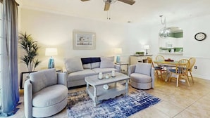 A living room with a sofa, armchairs, a coffee table, a ceiling fan, and a dining area with a table and chairs. - River Crossing Unit 124 (North Myrtle Beach)