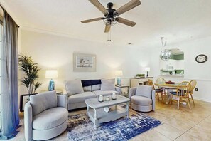 Ein Wohnzimmer mit einer Couch, Sesseln, einem Couchtisch, einem Deckenventilator und einem Essbereich mit Tisch und Stühlen.