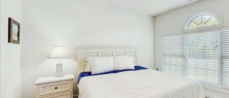 A bedroom with a bed, nightstand, lamp, ceiling fan, and a window with blinds.