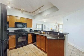 A kitchen with wooden cabinets, a black refrigerator, a microwave, an oven, and a sink. - Bahama Sands Unit PH02 (North Myrtle Beach)