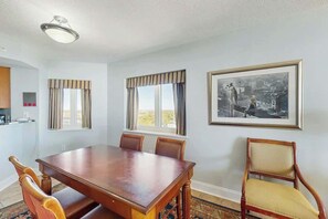 A dining area with a wooden table and chairs, a framed photograph on the wall, and a window with curtains. - Bahama Sands Unit PH02 (North Myrtle Beach)