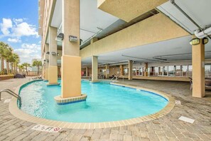 An indoor swimming pool with a tiled edge, surrounded by a brick floor and supported by concrete pillars. - Bahama Sands Unit PH02 (North Myrtle Beach)