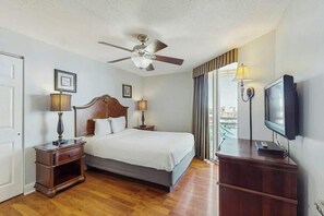 A hotel room with a bed, a ceiling fan, a television, and a view of the city through the window. - Bahama Sands Unit PH02 (North Myrtle Beach)