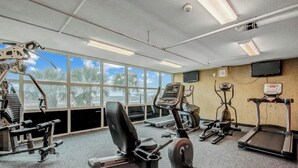 A gym with various exercise equipment, large windows, and a television on the wall. - Bahama Sands Unit PH02 (North Myrtle Beach)