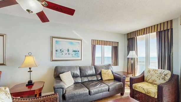 A living room with a leather sofa, a wicker chair, a wooden coffee table, and a ceiling fan. - Bahama Sands Unit PH02 (North Myrtle Beach)
