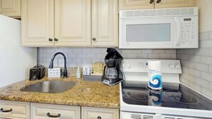 A kitchen with beige cabinets, a granite countertop, a white microwave, a stove, a coffee maker, and a toaster. - Bay Watch Resort 0339 (North Myrtle Beach)