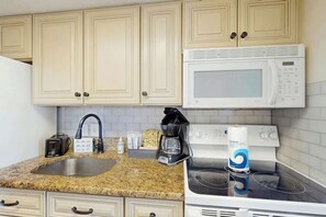 A kitchen with beige cabinets, a granite countertop, a white microwave, a stove, a coffee maker, and a toaster. - Bay Watch Resort 0339 (North Myrtle Beach)