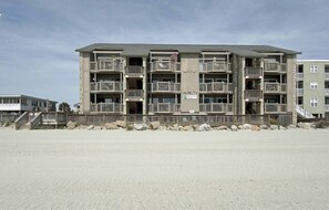A multi-story building with balconies, a sandy ground floor, and a clear sky. - Serenity Now Retreat (Murrells Inlet)