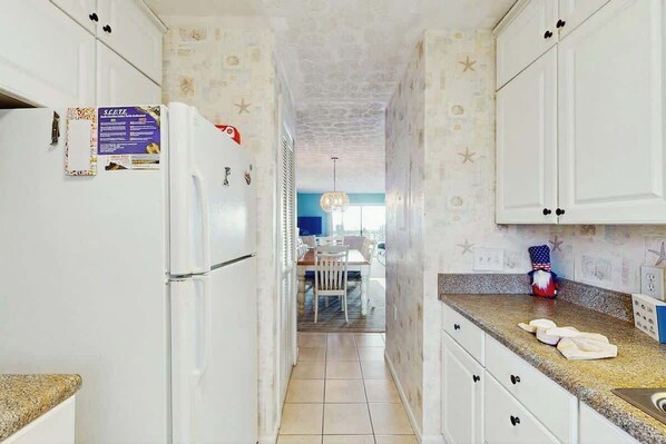 A narrow kitchen with white cabinets, a refrigerator, and a countertop with a sink. - Serenity Now Retreat (Murrells Inlet)