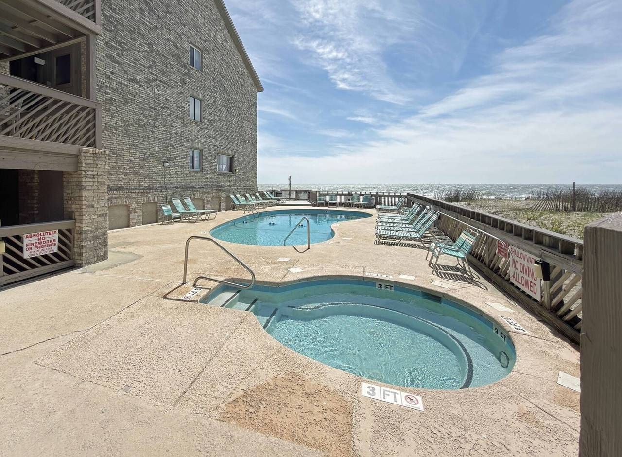 A pool area with two pools, a wooden deck, and a building with a stone facade.