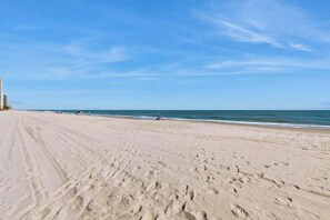 A wide sandy beach with footprints, a clear sky, and a distant shoreline. - Serenity Now Retreat (Murrells Inlet)