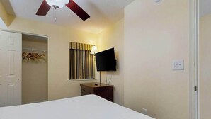 Et hotelværelse med seng, ventilator, tv ophængt på væggen og et garderobeskab.