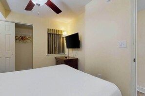 Ein Hotelzimmer mit einem Bett, einem Deckenventilator, einem an der Wand befestigten Fernseher und einem Kleiderschrank.