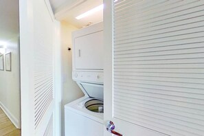 Un lavadero con lavadora y secadora apiladas, una puerta con manija y una lámpara sobre la secadora.