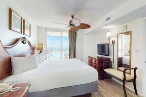 Ein Hotelzimmer mit einem großen Bett, einem Fernseher, einem Schreibtisch, einem Sessel und Meerblick.