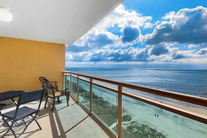 Ein Balkon mit Glasgeländer, der auf ein Gewässer und einen wolkenlosen Himmel blickt.