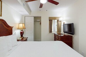 Ein Hotelzimmer mit einem Bett, einem Fernseher, einem Schreibtisch mit Lampe, einem Kleiderschrank und einem Deckenventilator.