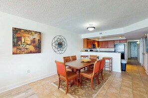 Ein Essbereich mit einem Holztisch und Stühlen, eine Küche im Hintergrund und ein Bild an der Wand.
