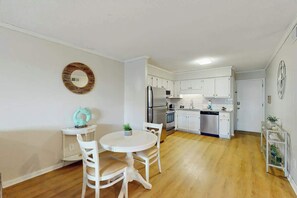 Cocina compacta con muebles blancos, un refrigerador de acero inoxidable y un comedor con una mesa redonda y sillas.