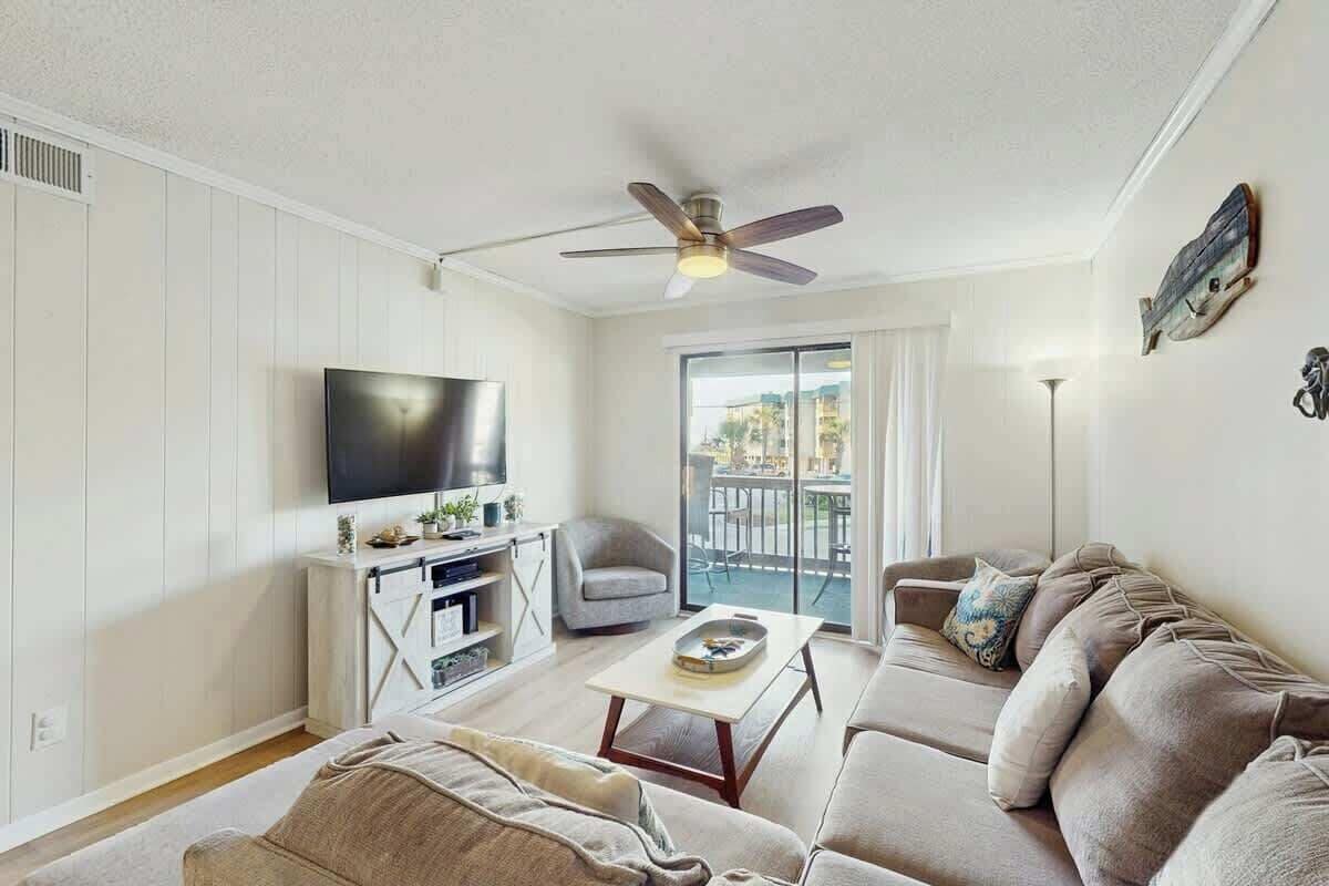 Ein Wohnzimmer mit Fernseher, Deckenventilator, Sofa und einer Schiebetür zu einem Außenbereich.