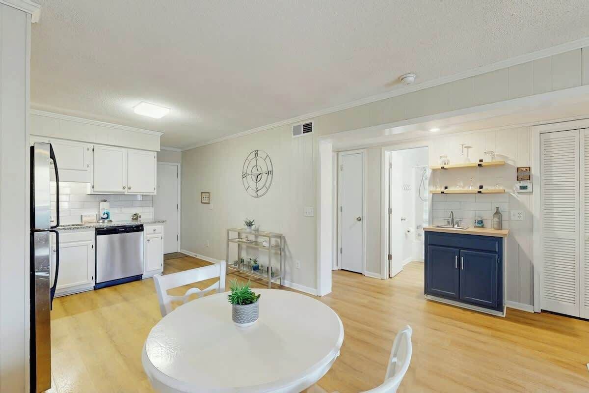 A modern kitchen with white cabinets, a stainless steel refrigerator, and a dining area with a round table and chairs.