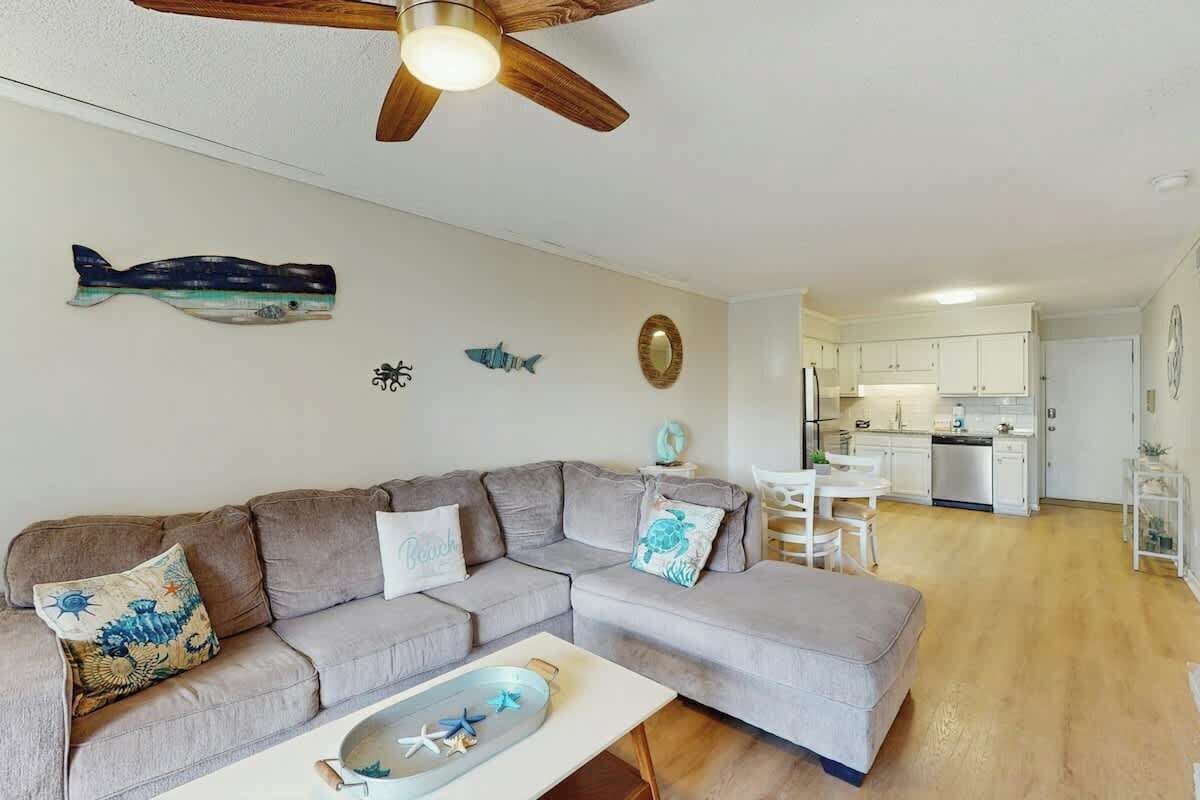Una sala de estar con un sofá seccional gris, un ventilador de techo y un cuadro de peces decorativos.