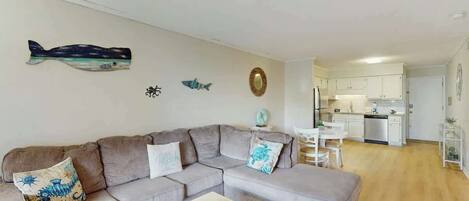 Una sala de estar con un sofá seccional gris, un ventilador de techo y un cuadro de peces decorativos.