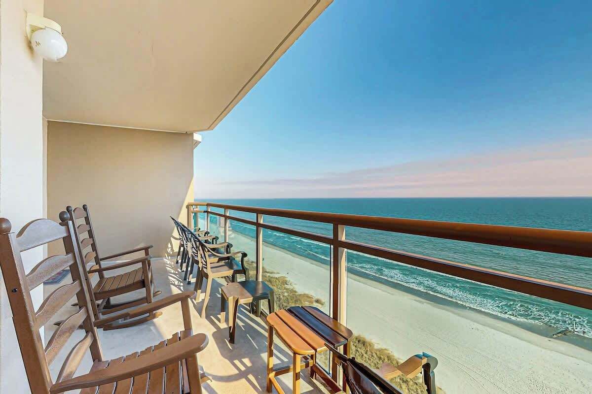 A balcony with wooden furniture overlooking a beach.