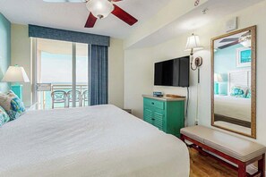 A hotel room with a large bed, a TV, a mirror, a bench, and a view of the outdoors.