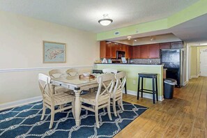 A dining area with a wooden table and chairs, a kitchen with wooden cabinets, and a black trash bin.