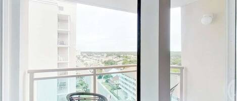 Un balcón con una silla, barandilla y vistas a un edificio y follaje.