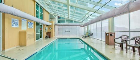 Piscina interior con techos de vidrio transparente, señalización de seguridad y zonas de estar.