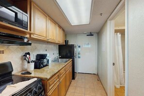 A compact kitchen with a stove, microwave, and refrigerator, wooden cabinets, and a tiled backsplash. - Compass Cove Unit 560 (Myrtle Beach)