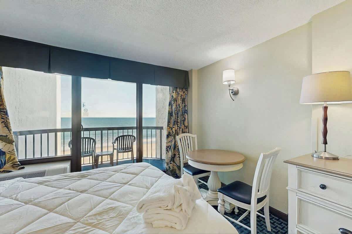 A hotel room with a bed, a desk, a chair, a table, and a view of the ocean.
