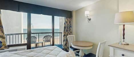 Ett hotellrum med en säng, ett skrivbord, en stol, ett bord och utsikt över havet.