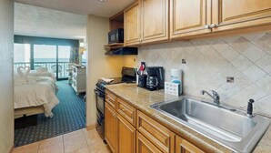 A compact hotel kitchen with wooden cabinets, a stainless steel sink, and a microwave. - Compass Cove Unit 560 (Myrtle Beach)