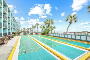 Ein Shuffleboard-Spielfeld neben einem Gebäude mit Balkonen, Palmen und blauem Himmel.