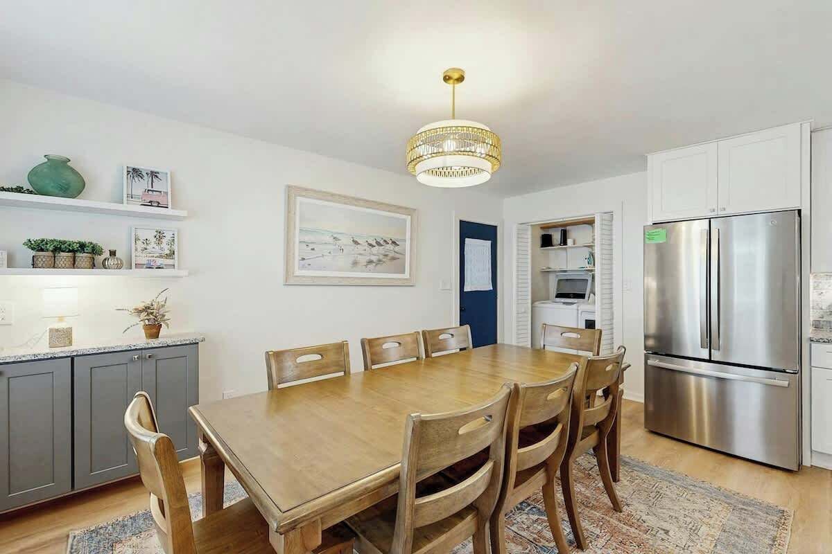 A modern kitchen with a dining table, chairs, a chandelier, and a stainless steel refrigerator.