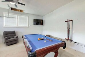 A pool table with a blue felt surface, a grey armchair, and a television mounted on the wall. - Cherry Grove Beach Retreat (North Myrtle Beach)